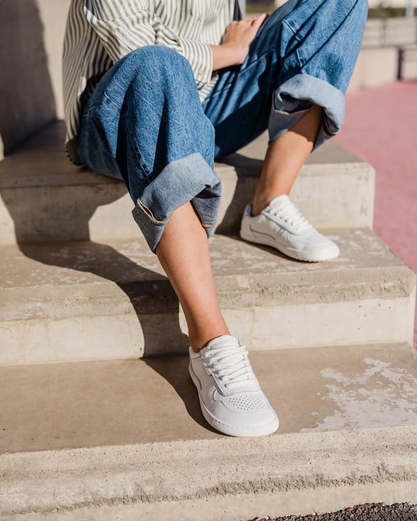 A person sitting on concrete steps wearing blue cuffed jeans, a striped shirt, and white low-top sneakers in bright outdoor light.