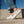 White leather low-top sneakers worn with cuffed blue jeans, shown outdoors on concrete steps under a clear blue sky.
